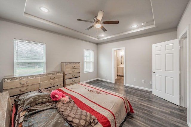 bedroom featuring connected bathroom, a tray ceiling, dark wood-type flooring, and ceiling fan