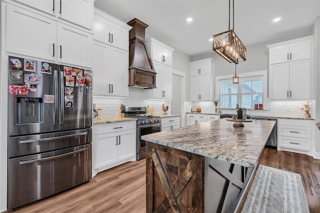 kitchen featuring decorative light fixtures, stainless steel appliances, a center island, and white cabinets