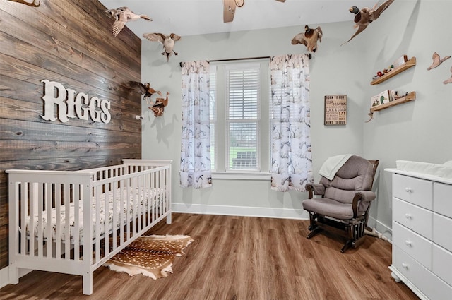 bedroom featuring hardwood / wood-style flooring, a crib, wooden walls, and ceiling fan