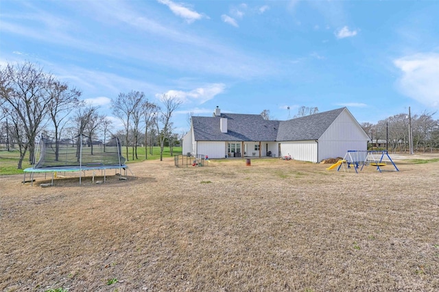 back of property featuring a trampoline, a lawn, and a playground