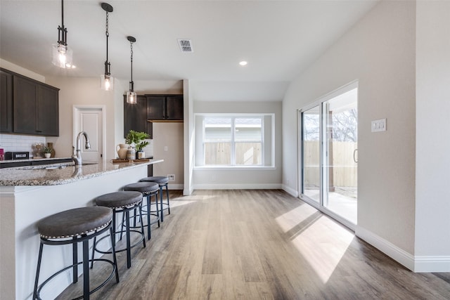 kitchen with visible vents, dark brown cabinets, light stone countertops, and light wood finished floors