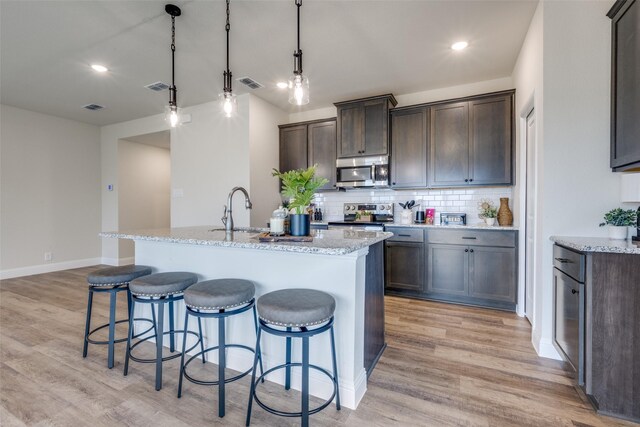 102 Walnut St, Whitesboro, TX 76273 - kitchen with stainless steel appliances, light wood finished floors, a kitchen island with sink, decorative backsplash, and recessed lighting