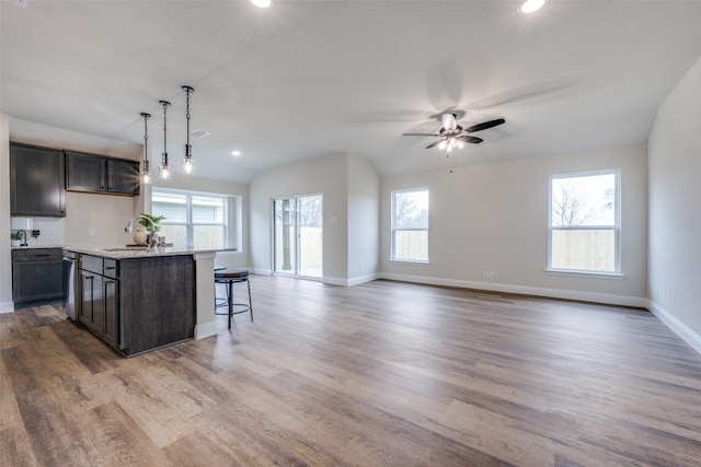 kitchen with hardwood / wood-style floors, pendant lighting, sink, a kitchen island with sink, and light stone counters