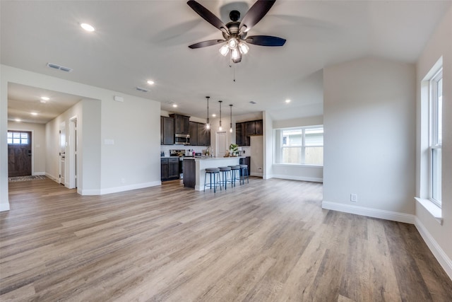 unfurnished living room featuring a ceiling fan, baseboards, a healthy amount of sunlight, and light wood-style flooring