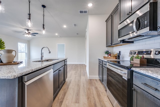 kitchen featuring sink, tasteful backsplash, appliances with stainless steel finishes, pendant lighting, and light stone countertops