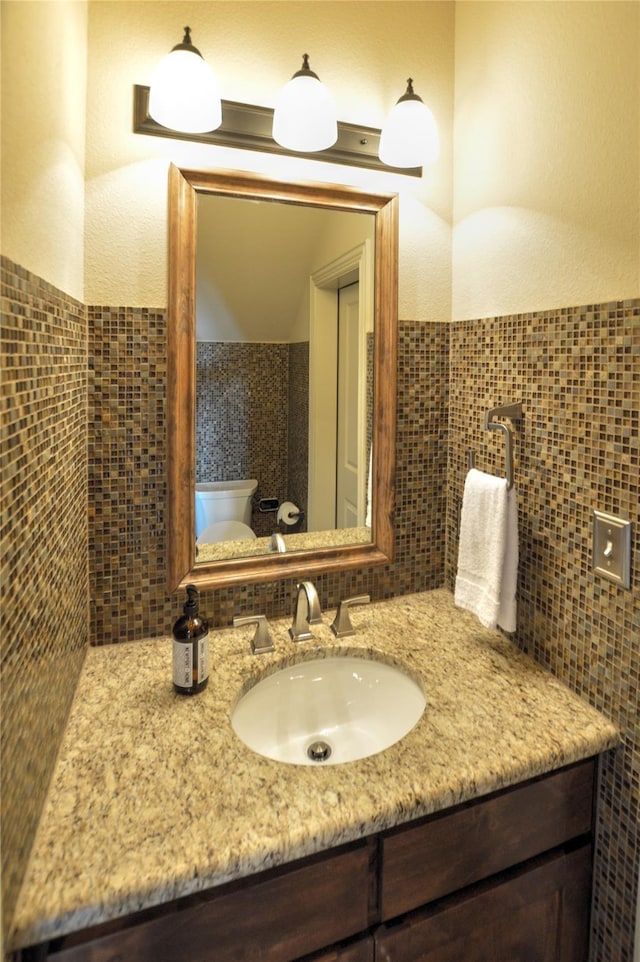 bathroom with vanity, toilet, and tile walls