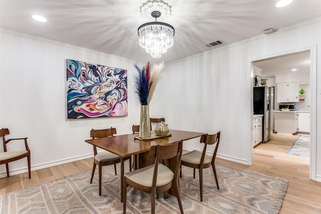 dining area featuring visible vents, baseboards, ornamental molding, light wood finished floors, and an inviting chandelier