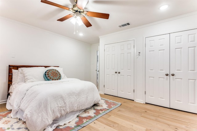 bedroom with light wood finished floors, visible vents, baseboards, crown molding, and two closets