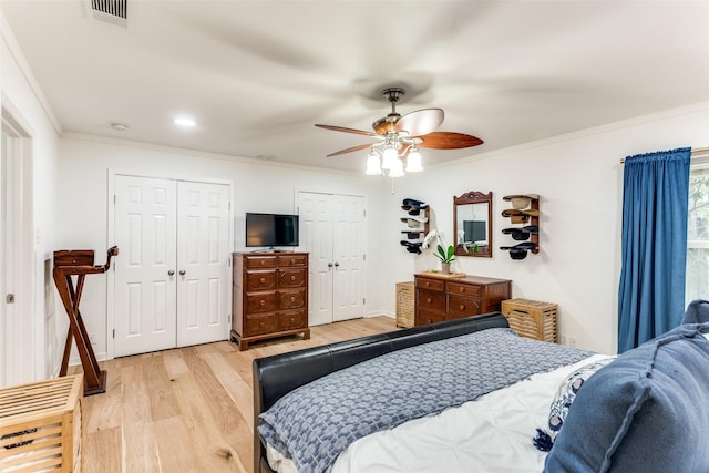 bedroom featuring light wood finished floors, visible vents, ceiling fan, ornamental molding, and multiple closets