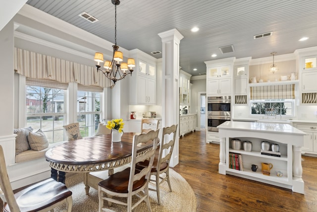 dining room with sink, crown molding, an inviting chandelier, dark hardwood / wood-style flooring, and ornate columns