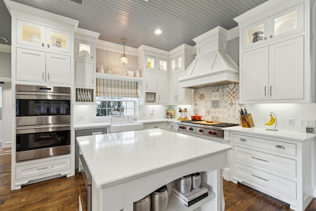 kitchen featuring white cabinetry, appliances with stainless steel finishes, decorative light fixtures, and custom range hood