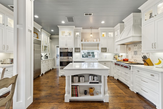 kitchen with stainless steel appliances, premium range hood, white cabinets, and decorative light fixtures