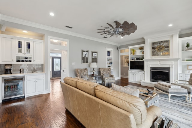 living room featuring indoor wet bar, wine cooler, dark hardwood / wood-style flooring, ceiling fan, and crown molding