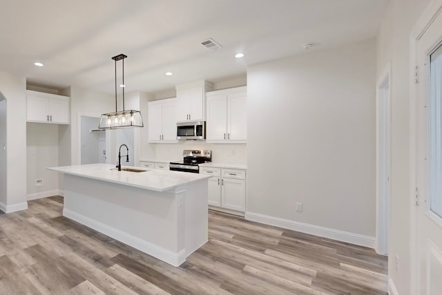 kitchen featuring sink, decorative light fixtures, appliances with stainless steel finishes, a kitchen island with sink, and white cabinets