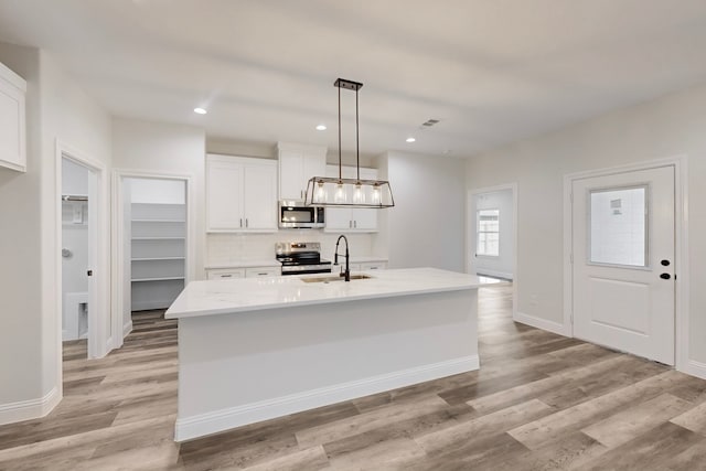 kitchen with appliances with stainless steel finishes, decorative light fixtures, white cabinetry, sink, and a kitchen island with sink