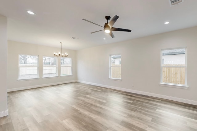 spare room with ceiling fan with notable chandelier and light wood-type flooring