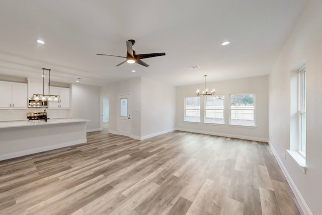 unfurnished living room with sink, ceiling fan with notable chandelier, and light hardwood / wood-style flooring