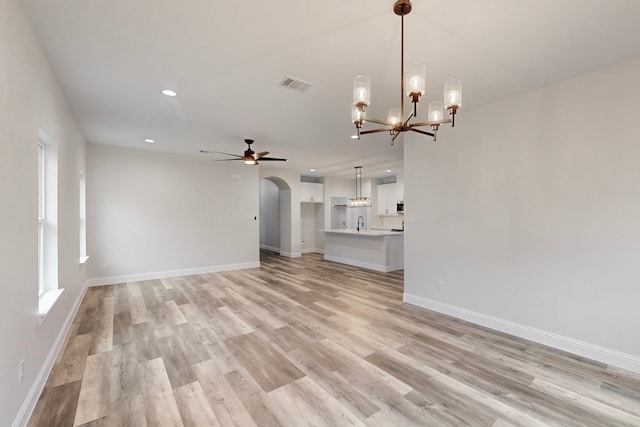 unfurnished living room with sink, ceiling fan with notable chandelier, and light wood-type flooring