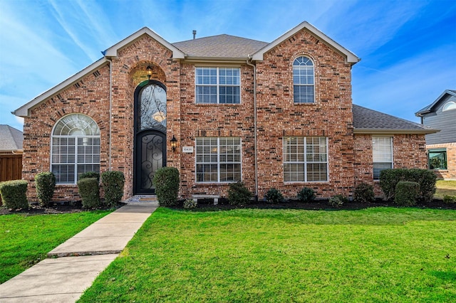 traditional-style home with a shingled roof, a front lawn, and brick siding