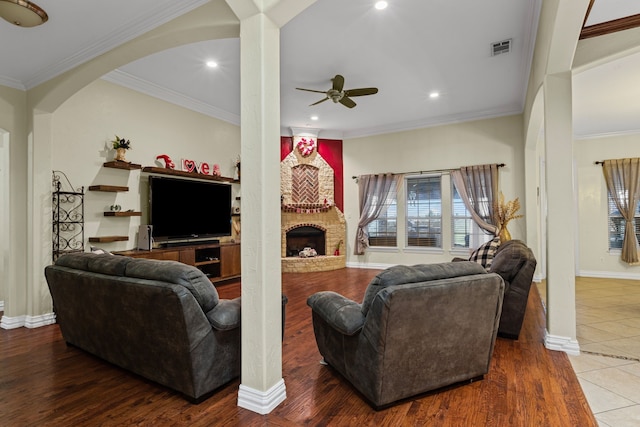 living room featuring ceiling fan, ornamental molding, hardwood / wood-style floors, and a brick fireplace