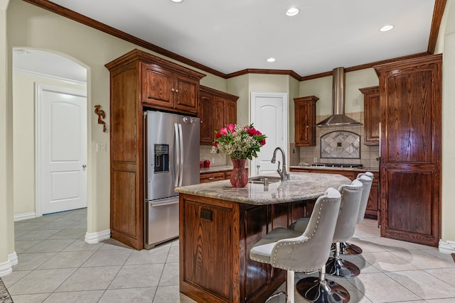kitchen featuring sink, appliances with stainless steel finishes, a kitchen island with sink, light stone countertops, and wall chimney exhaust hood