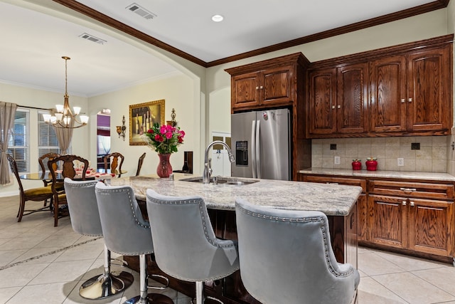 kitchen featuring decorative light fixtures, sink, light tile patterned floors, stainless steel fridge with ice dispenser, and a center island with sink