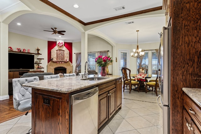 kitchen with appliances with stainless steel finishes, decorative light fixtures, sink, light stone counters, and a center island with sink