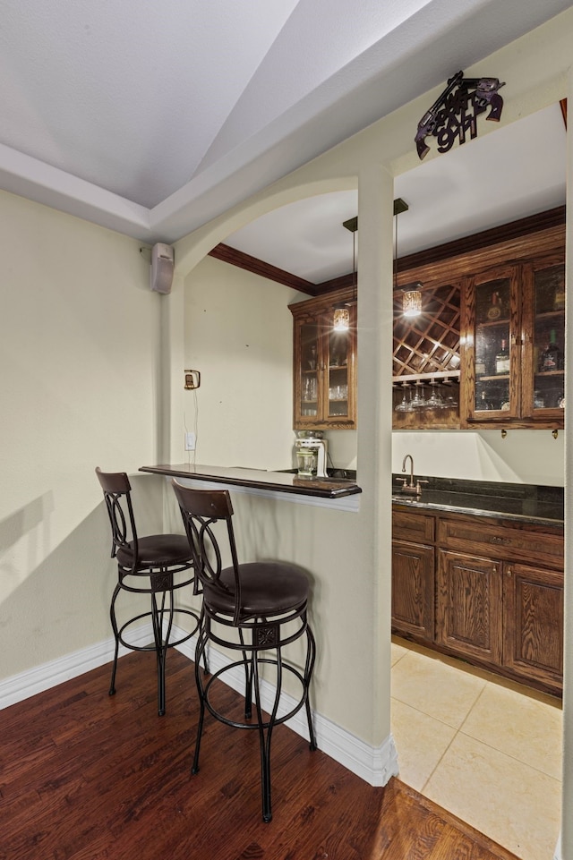 bar with pendant lighting, vaulted ceiling, light hardwood / wood-style floors, and dark brown cabinetry