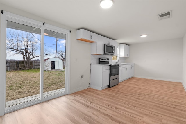 kitchen featuring white cabinetry, backsplash, light wood-type flooring, and appliances with stainless steel finishes