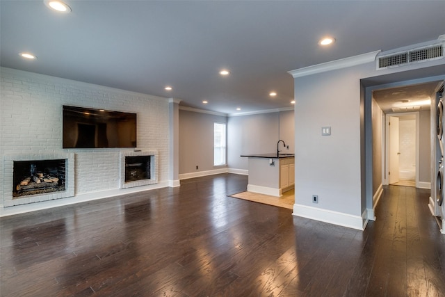 unfurnished living room featuring dark wood-type flooring, crown molding, sink, and a brick fireplace