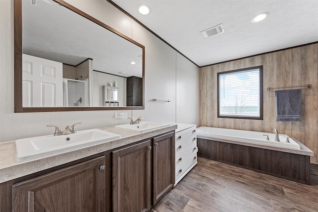 bathroom with independent shower and bath, wood-type flooring, ornamental molding, vanity, and a textured ceiling