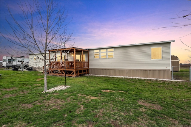 back house at dusk with a deck and a lawn