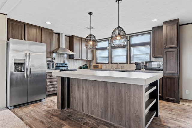 kitchen featuring a kitchen island, decorative light fixtures, stainless steel fridge, dark brown cabinets, and wall chimney exhaust hood