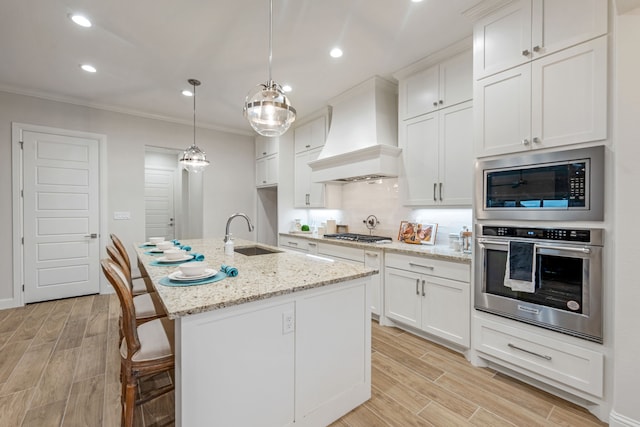 kitchen with sink, appliances with stainless steel finishes, white cabinetry, a center island with sink, and custom exhaust hood