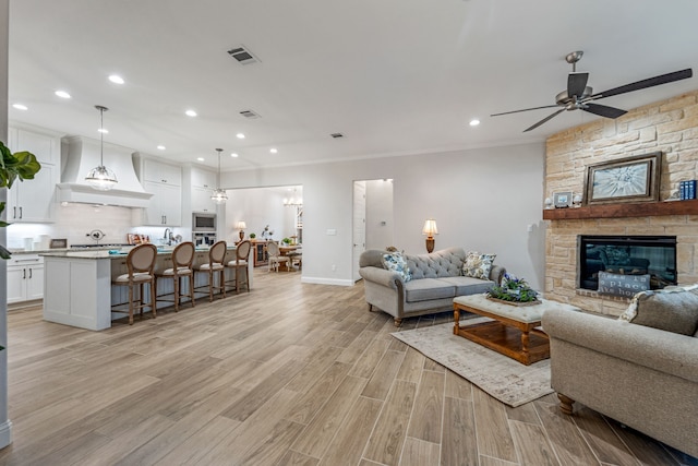 living room featuring crown molding, ceiling fan, a stone fireplace, and light hardwood / wood-style flooring