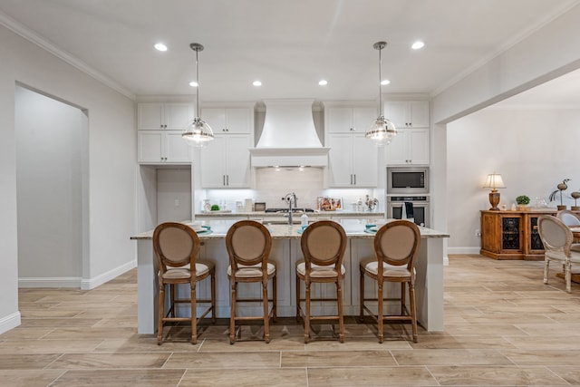 kitchen with appliances with stainless steel finishes, white cabinets, a center island with sink, decorative light fixtures, and custom exhaust hood