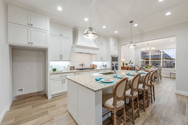 kitchen featuring pendant lighting, light stone counters, a center island with sink, and white cabinets