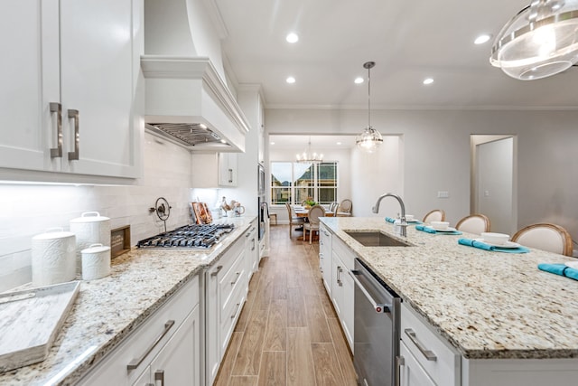 kitchen featuring sink, appliances with stainless steel finishes, a kitchen island with sink, white cabinets, and decorative light fixtures