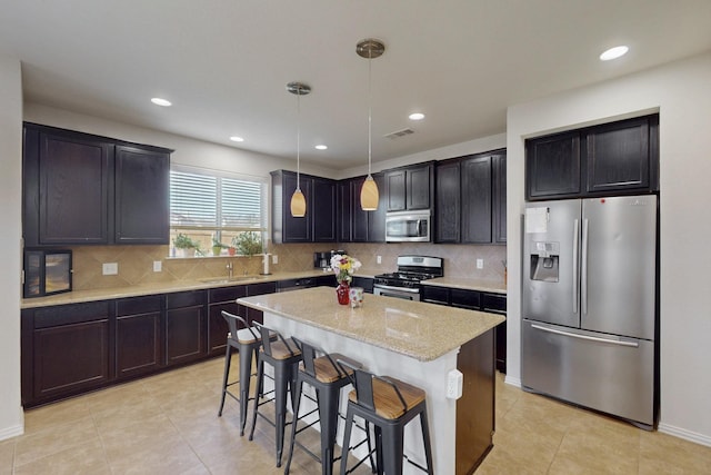 kitchen with hanging light fixtures, stainless steel appliances, a breakfast bar, a kitchen island, and sink