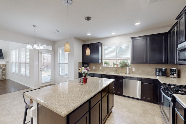 kitchen with appliances with stainless steel finishes, sink, backsplash, a kitchen island, and hanging light fixtures