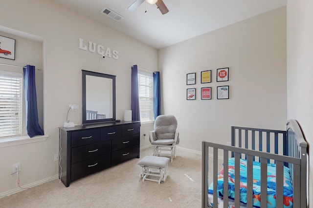 carpeted bedroom with ceiling fan and a nursery area