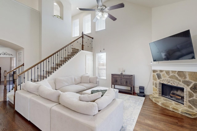 living room with ceiling fan, plenty of natural light, dark wood-type flooring, and a stone fireplace