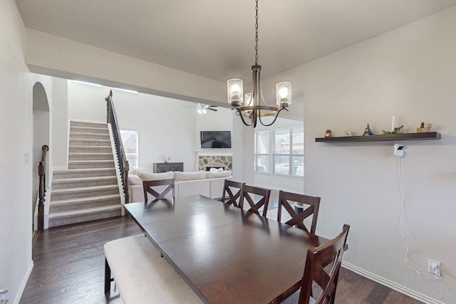 dining room featuring ceiling fan with notable chandelier, dark hardwood / wood-style flooring, and a fireplace