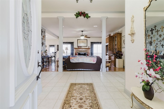 tiled foyer featuring ornate columns, a brick fireplace, crown molding, and ceiling fan