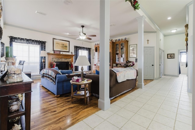 living room with light hardwood / wood-style flooring, ceiling fan, crown molding, a fireplace, and ornate columns