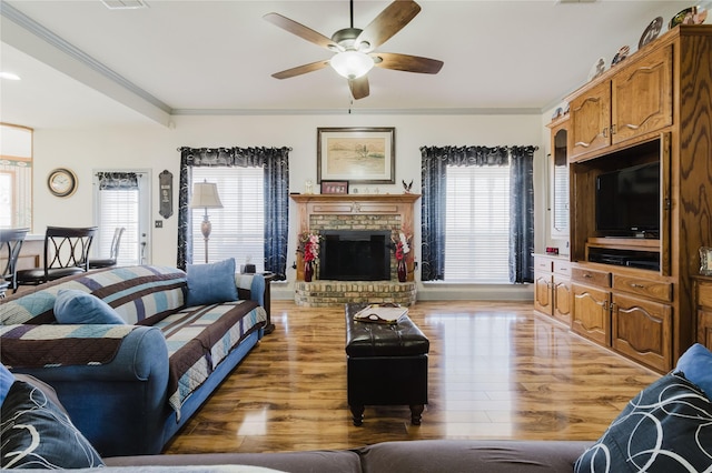 living room featuring ceiling fan, light hardwood / wood-style flooring, crown molding, and a fireplace