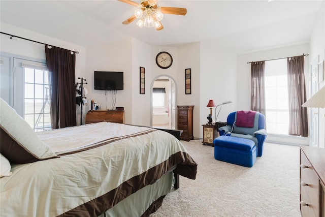 carpeted bedroom with ensuite bathroom, multiple windows, and ceiling fan