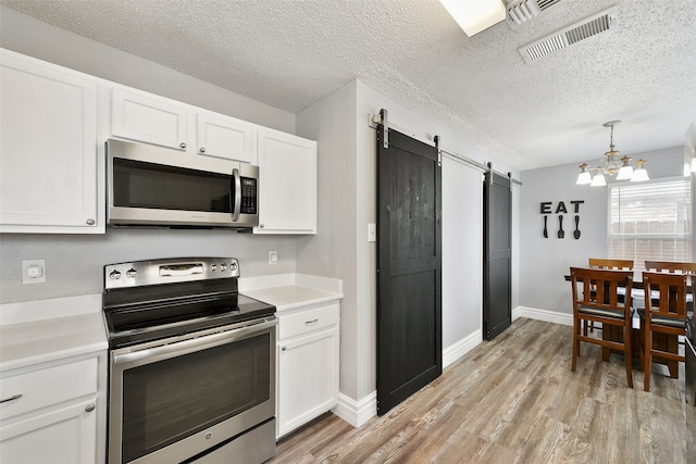728 Oriole Dr, Saginaw, TX 76131 - kitchen featuring appliances with stainless steel finishes, light countertops, white cabinetry, and a barn door