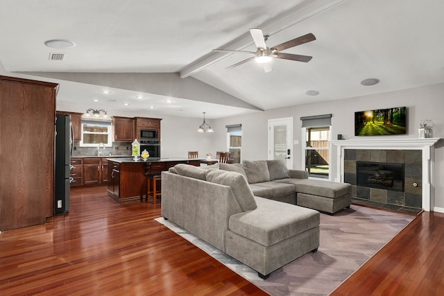 living room featuring visible vents, dark wood-type flooring, lofted ceiling with beams, ceiling fan, and a tile fireplace