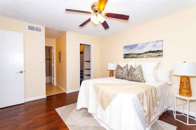 bedroom with ceiling fan, dark hardwood / wood-style flooring, a textured ceiling, and a spacious closet